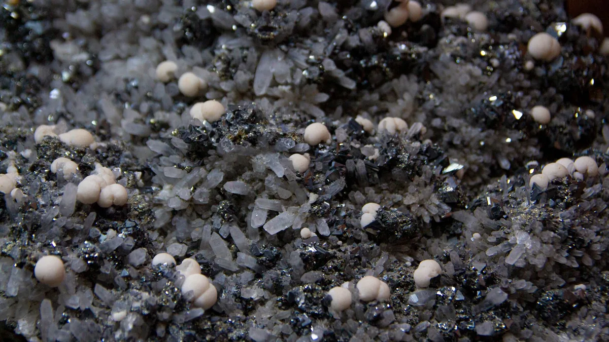 Detailed photograph of mineral crystals with metallic shine and small white spheres.